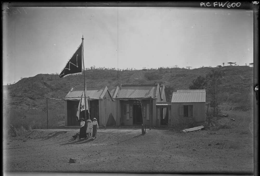 [Three women near three small buildings with Chinese writing and flag] [picture]