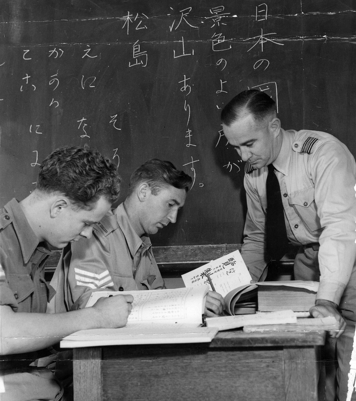 Sq Ldr M.A. WIADROWSKI chief instructor of Language School at Point Cook checks over the work of Cpl. C.L. FUNCH & Sgt. J.J. COTTER (NZ) on the Jap Text Books [picture]